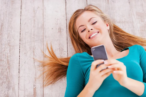 Young woman lying on the floor and holding phone — Stock Photo, Image