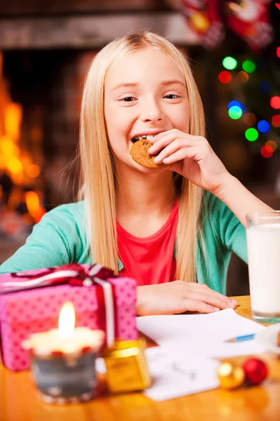 Menina comendo um biscoito perto da árvore de Natal — Fotografia de Stock