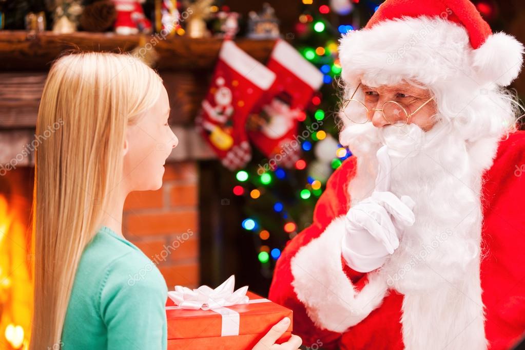 Little girl holding gift box and looking at Santa Claus