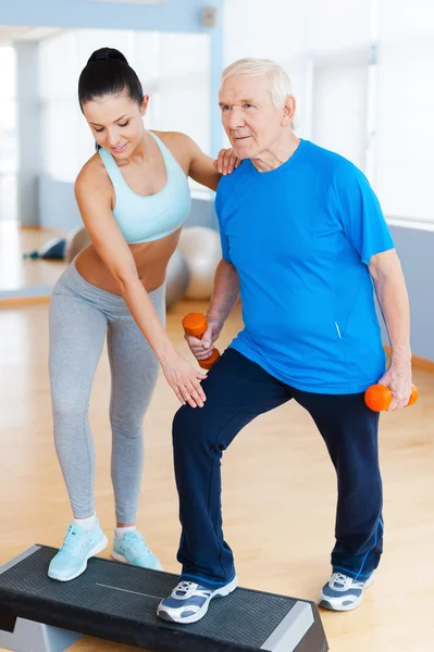 Można to zrobić! Pełna długość pewność kobiece fizjoterapeuta współpracuje z starszy mężczyzna w klubie zdrowia — Zdjęcie stockowe