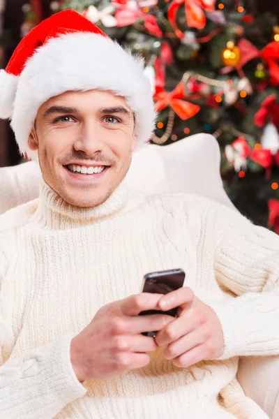 Mann mit Weihnachtsmannmütze textet auf seinem Handy — Stockfoto