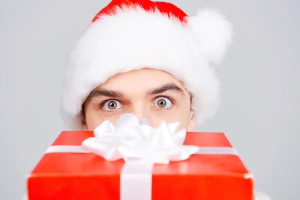 Mann mit Weihnachtsmütze versteckt Gesicht hinter Geschenkbox — Stockfoto