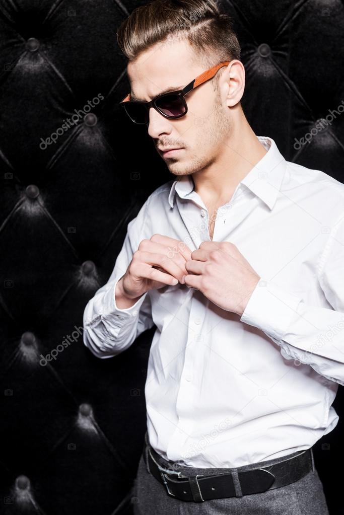 Man in sunglasses buttoning shirt