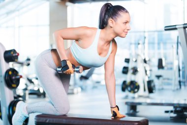 Spor salonunda dambıllarla egzersiz yapan bir kadın.