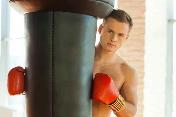 Boxer in sports gloves leaning at the punching bag — Stock Photo, Image