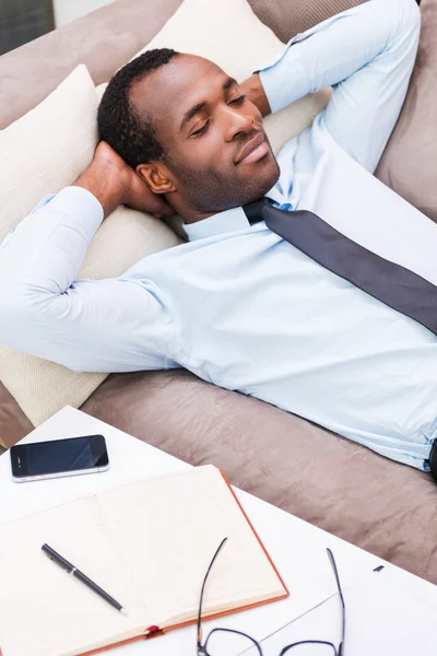 Africano homem de camisa e gravata deitado no sofá — Fotografia de Stock