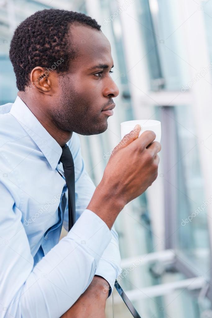 Thoughtful African man holding coffee