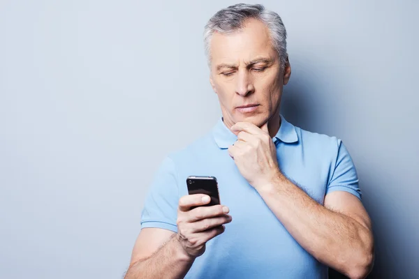 Älterer Mann im T-Shirt hält Handy in der Hand — Stockfoto