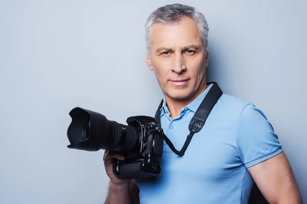 Mature man in T-shirt holding camera — Stock Photo, Image