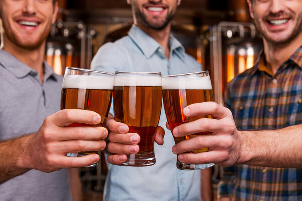 Young men stretching out glasses with beer