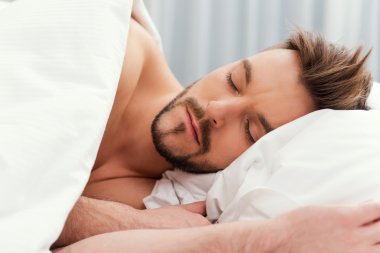 Gömleksiz adam yatakta uyuyor