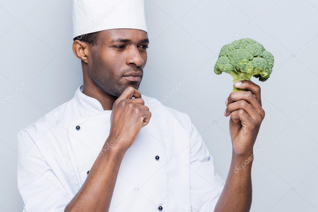 Thoughtful African chef holding broccoli