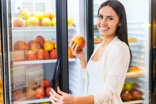 Mulher sorridente que toma maçã do refrigerador — Fotografia de Stock