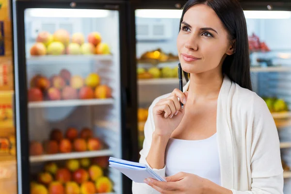 Femme réfléchie tenant liste d'achats — Photo