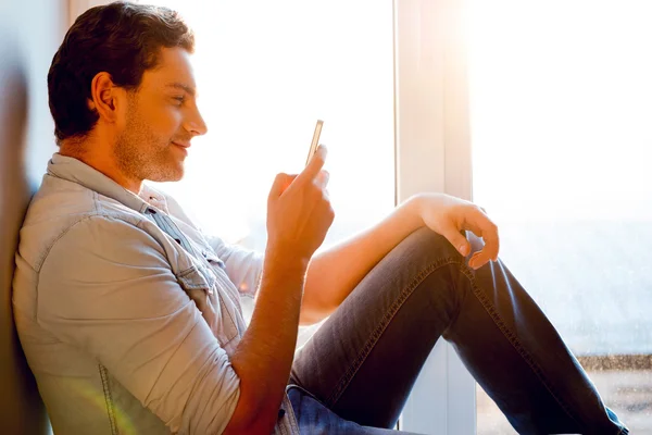 Az ember ül az ablakpárkányon, mobil telefon — Stock Fotó
