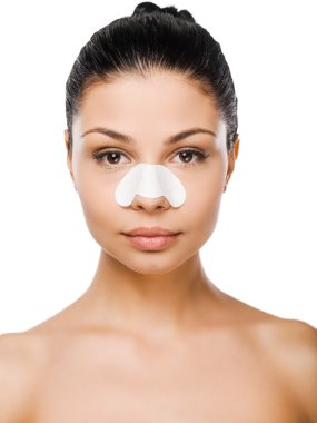 Cleaning her face. Beautiful young woman with clear-up patches on her nose looking at camera while standing against white background clipart