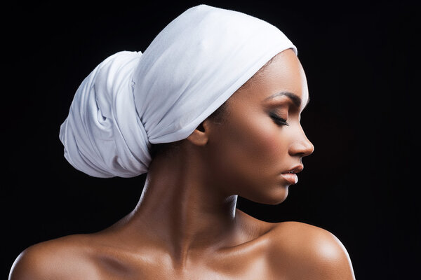 Beautiful African woman wearing a headscarf and keeping eyes closed while standing against black background