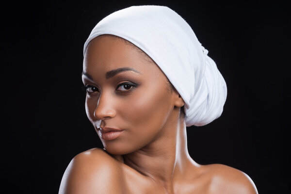 Beautiful African woman wearing a headscarf and looking at camera while standing against black background
