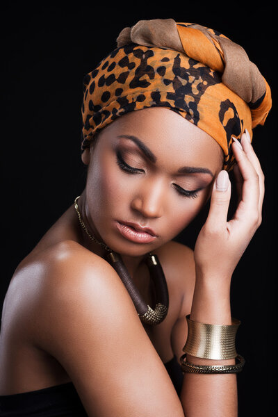 Beautiful African woman wearing a headscarf and touching head while standing against black background