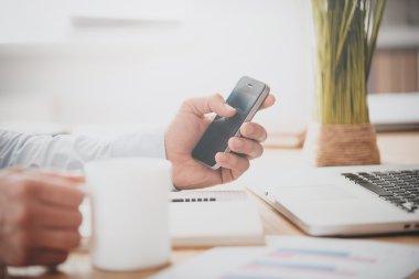 Cep telefonu ve kahve fincanı tutan adam