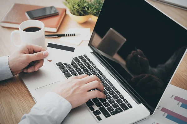 Homem trabalhando no laptop e segurando cartão de crédito — Fotografia de Stock