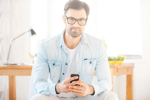 Człowiek w koszuli i okulary trzymając telefon komórkowy — Zdjęcie stockowe