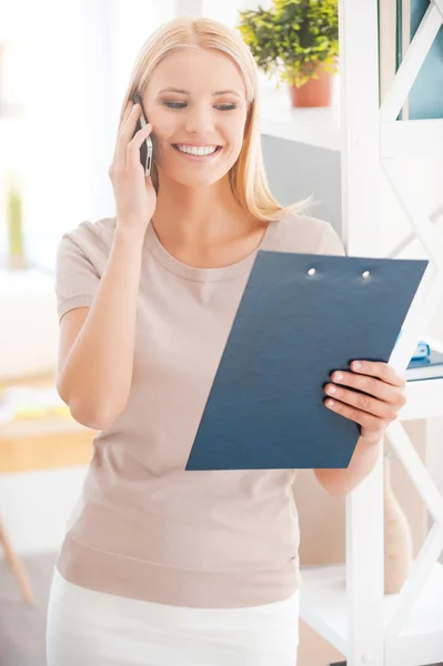 Woman talking on phone and looking at clipboard — Stock Photo, Image