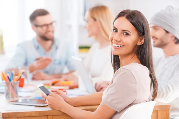 Woman looking over shoulder and holding mobile phone — Stock Photo, Image