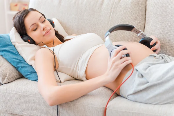 Gravid kvinna med hörlurar på magen — Stockfoto