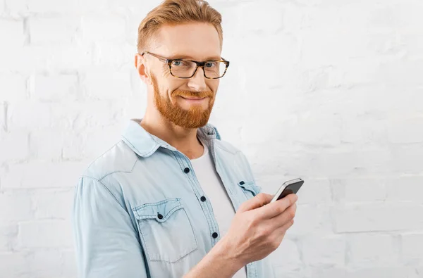 Молодий бородатий чоловік тримає мобільний телефон — стокове фото