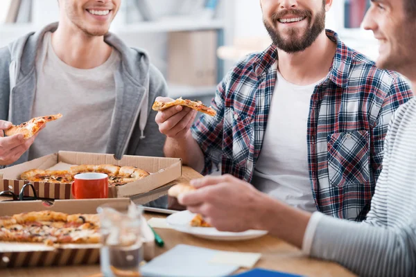 Hombres comiendo pizza mientras están sentados en el escritorio —  Fotos de Stock