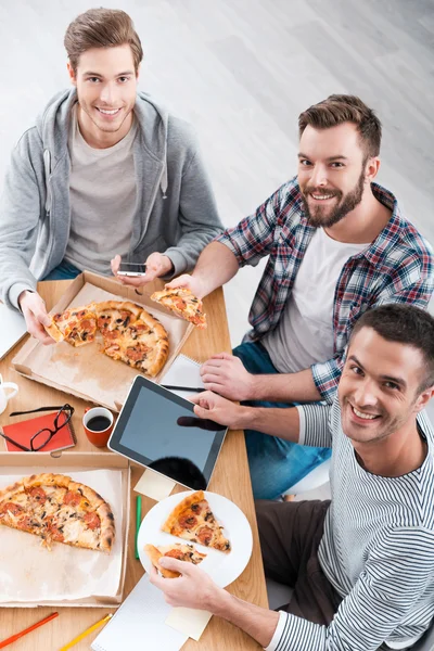 Homens comendo pizza enquanto sentados na mesa — Fotografia de Stock