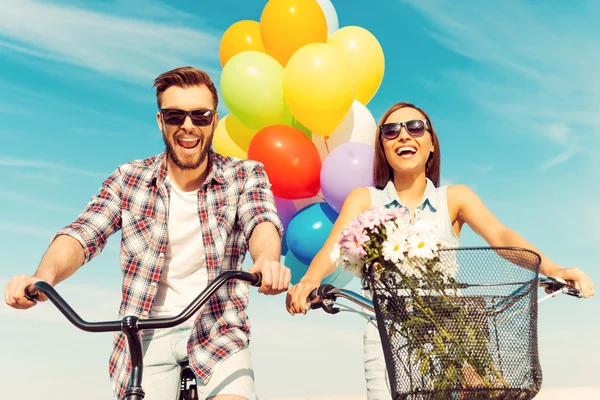 Couple riding on bicycles with colorful balloons — Stock Photo, Image