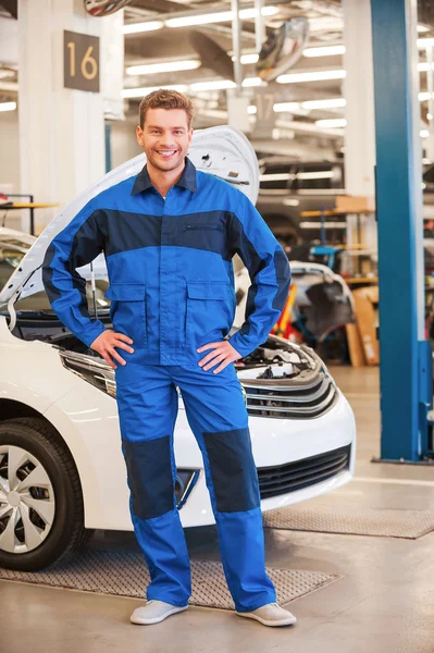 Young man standing in workshop with car — Stock Photo, Image