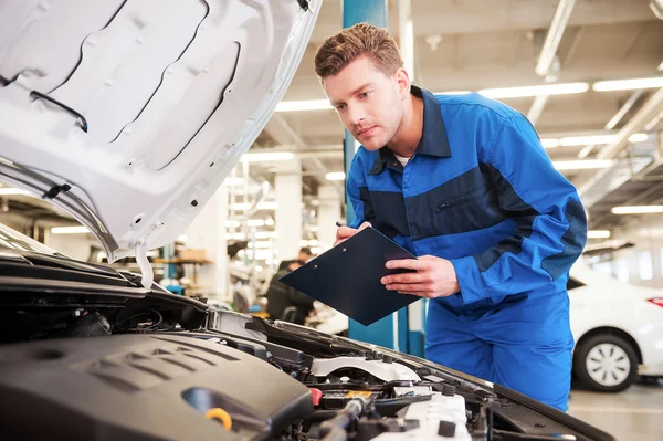 Hombre en uniforme examinando coche en taller —  Fotos de Stock