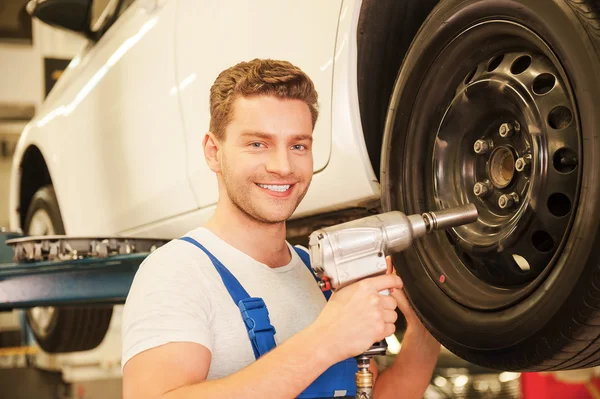 Hombre en uniforme trabajando con neumático de coche — Foto de Stock