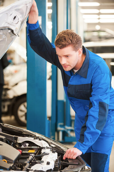 man in uniform examining car in workshop