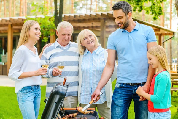 Family barbecuing meat on grill — Stock Photo, Image