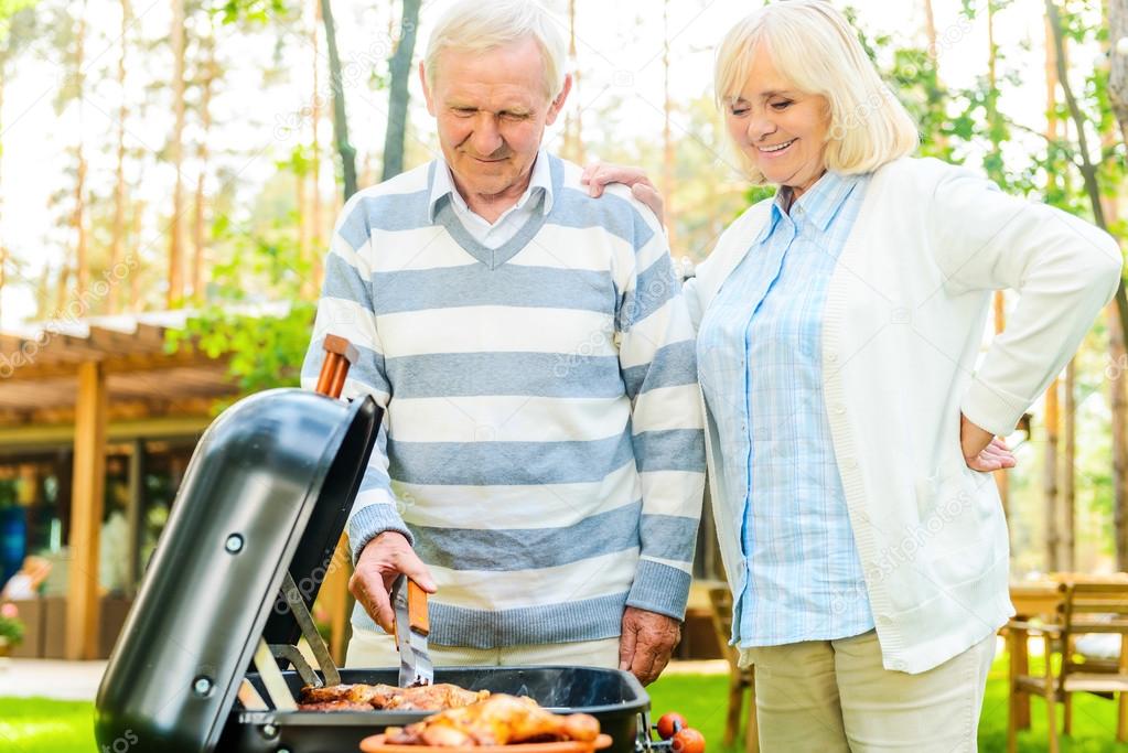 senior couple barbecuing meat on grill