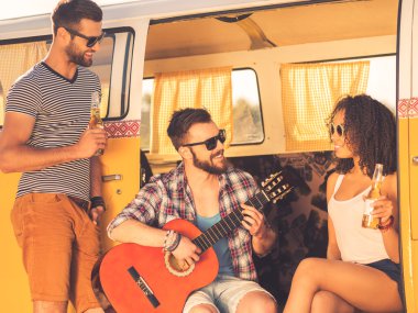 man sitting in minivan and playing guitar with friends