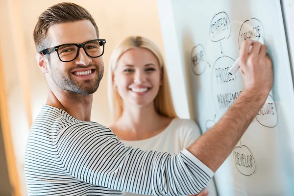 Man and woman standing near whiteboard in office — Stock Photo, Image