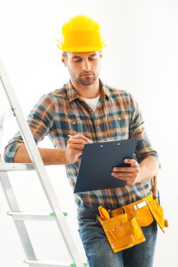 builder writing in clipboard and leaning at  ladder