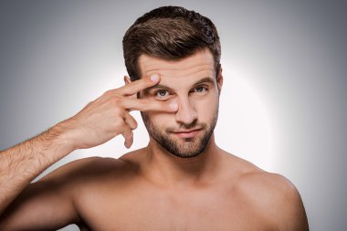 shirtless man holding fingers near his eye