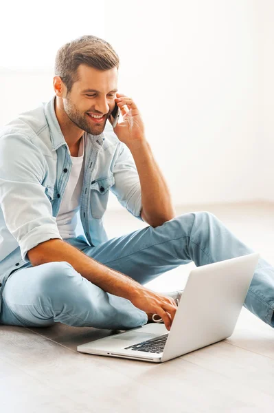 Hombre trabajando en el ordenador portátil y hablando en el teléfono móvil — Foto de Stock