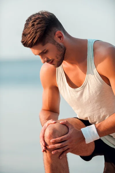 Schmerzen im Knie. Konzentrierter junger muskulöser Mann massiert Knie im Stehen — Stockfoto