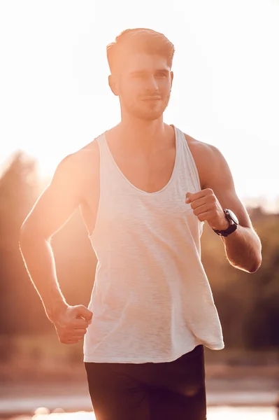 Muscular man running along riverbank — Stock Photo, Image