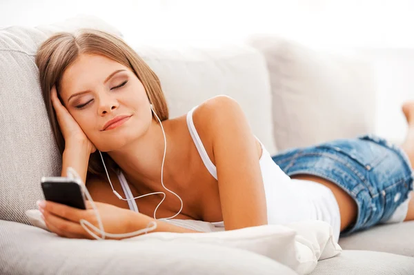 Woman in headphones holding phone on sofa — Stock Photo, Image