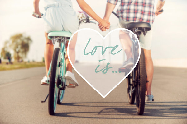 Love is... Rear view of young couple holding hands while riding on bicycles along the road