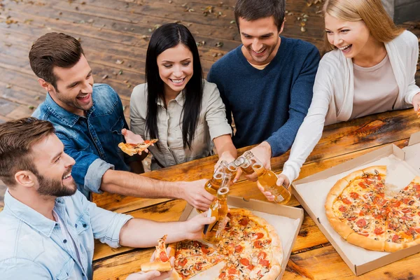 Personas tintinear botellas y comer pizza —  Fotos de Stock