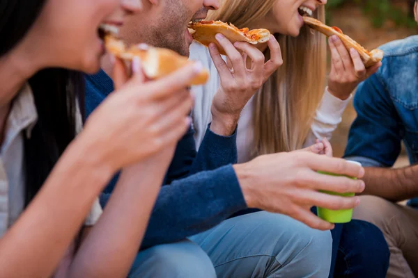 Молодые люди едят пиццу, сидя на открытом воздухе — стоковое фото